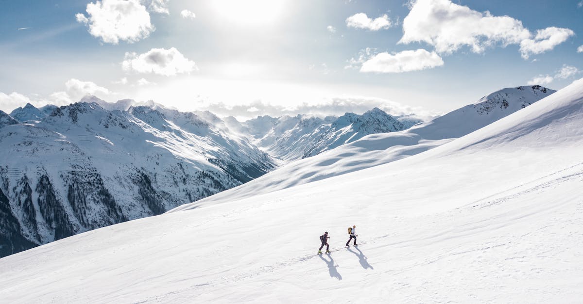 Two skiers climbing a sunlit snowy mountain slope in Ischgl, Austria, during winter.